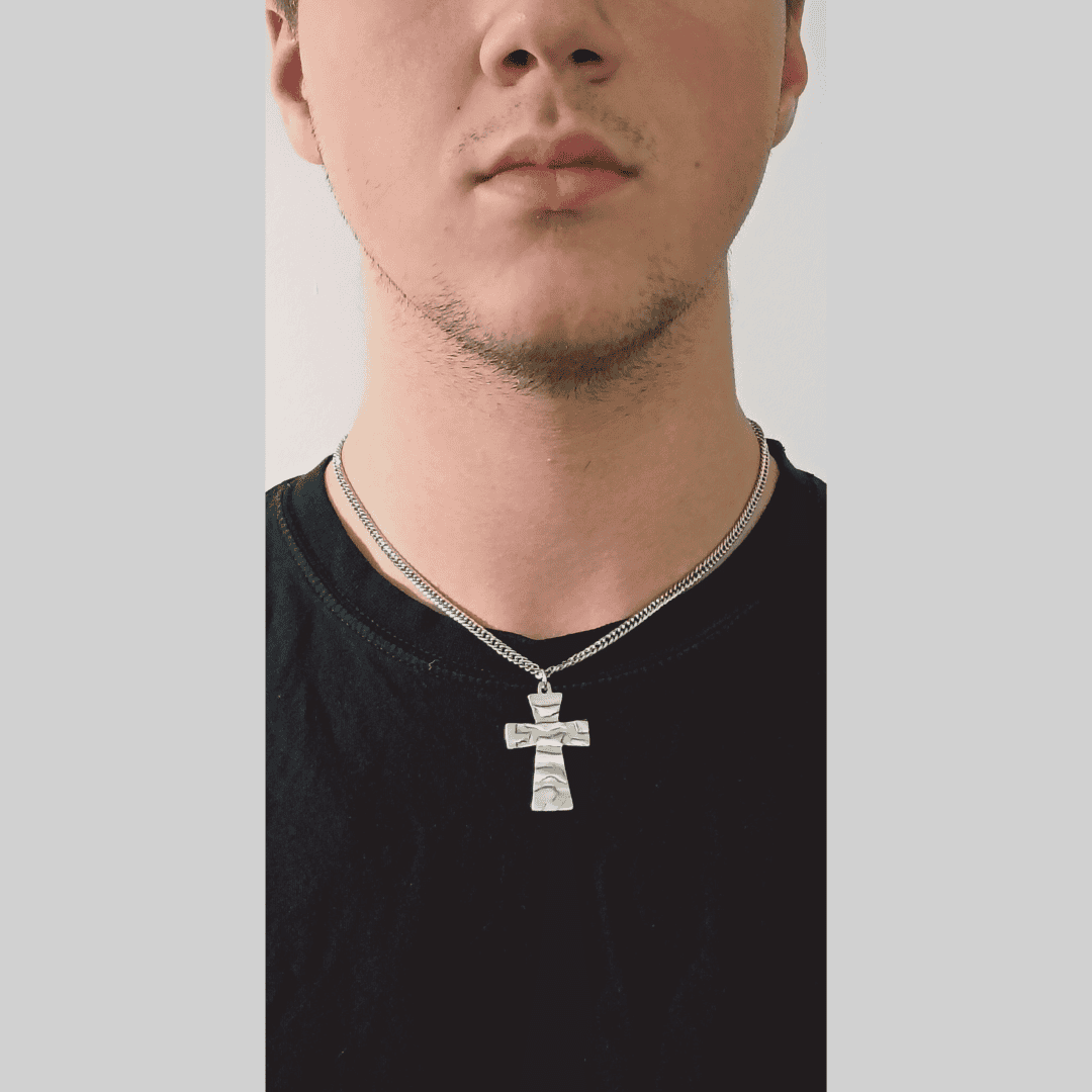 Man wearing a black shirt with a silver necklace featuring a cross pendant on a plain background