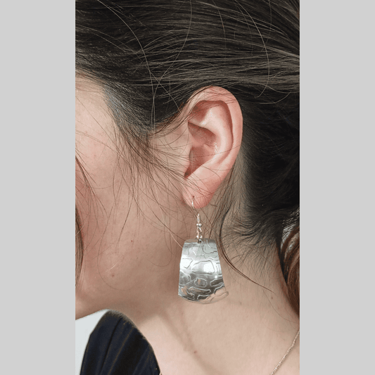Close-up of a person wearing a silver earring with a clear stone on a neutral background