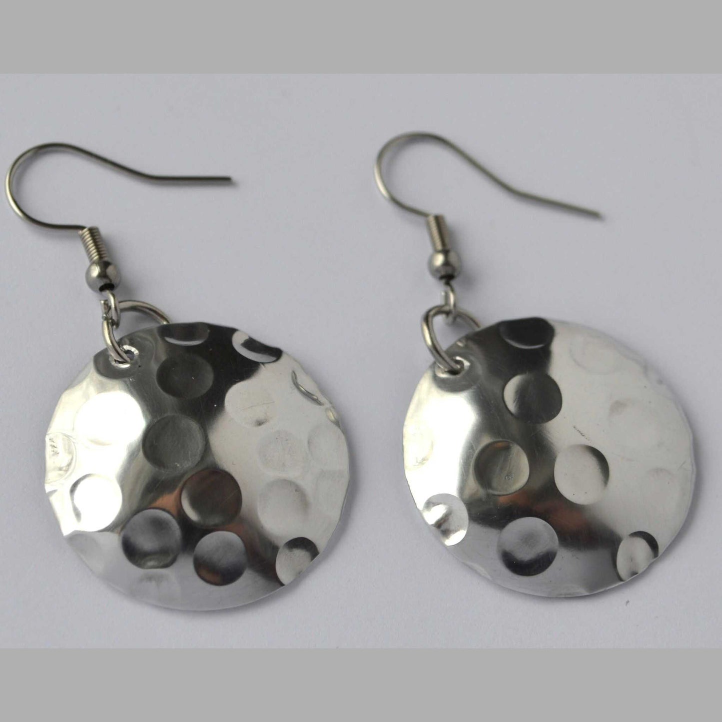 A pair of silver disc-shaped earrings with a hand-hammered texture and circular pattern design.