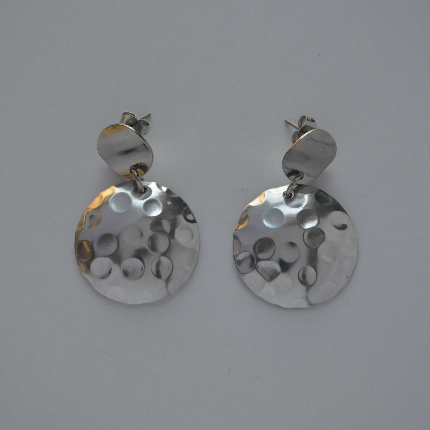 A pair of silver disc-shaped earrings with a hand-hammered texture and circular pattern design.