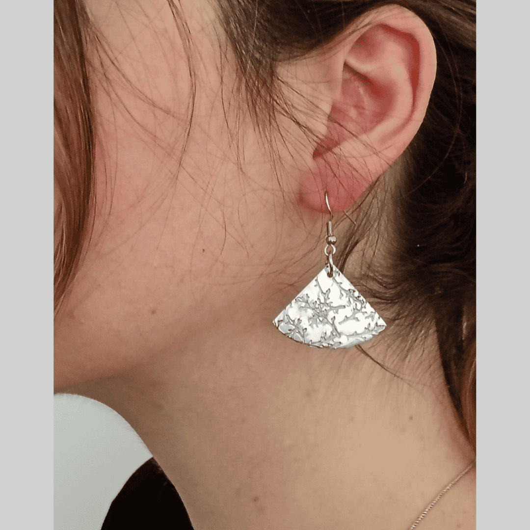 Silver fan-shaped earring worn by a person with a neutral background