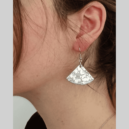 Silver fan-shaped earring worn by a person with a neutral background