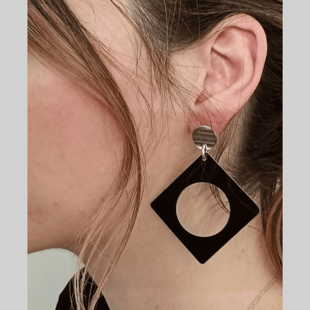 Black square earring with a circular cutout worn by a person.