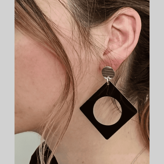 Black square earring with a circular cutout worn by a person.