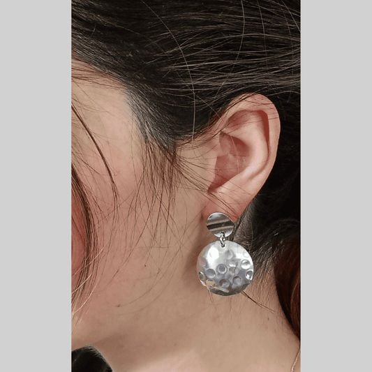 Close-up of a silver earring worn by a person with a neutral background