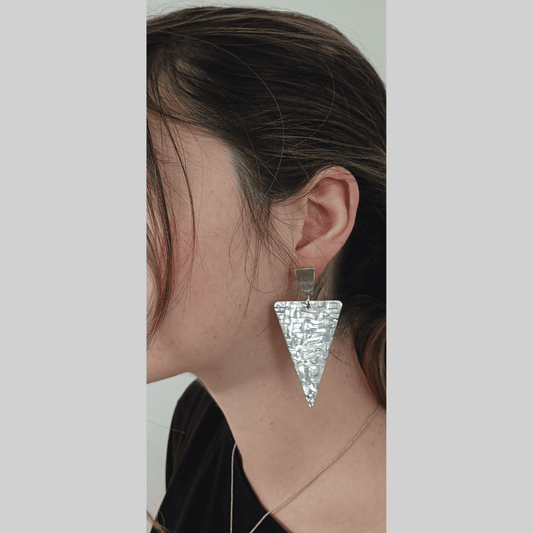 Person wearing a silver triangle-shaped earring on a plain background