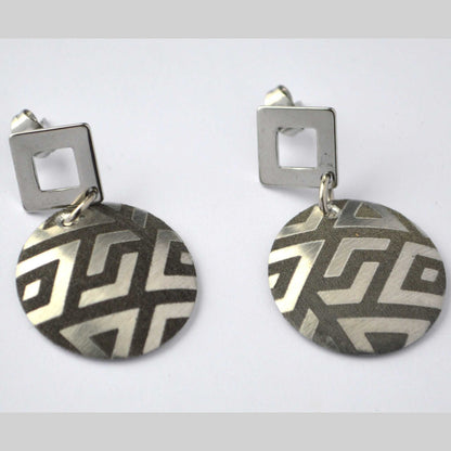 A pair of silver circular earrings with a triangular pattern, attached to a square post.