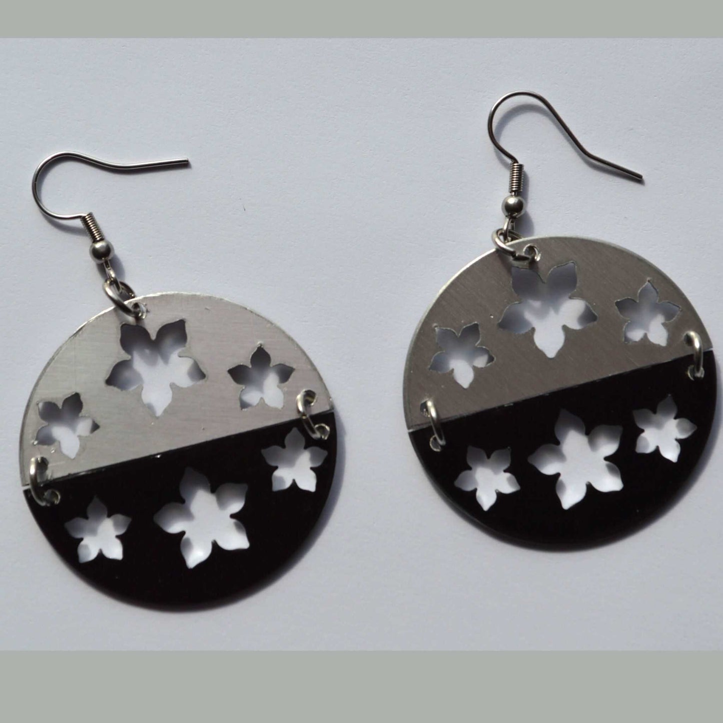 A pair of drop earrings made of black anodized aluminum with silver color accents, featuring flower cutouts.