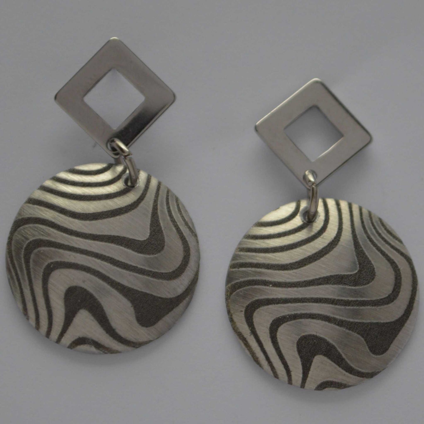 A pair of aluminum swirl design earrings with angled silhouettes, featuring a pattern of black and silver swirls.