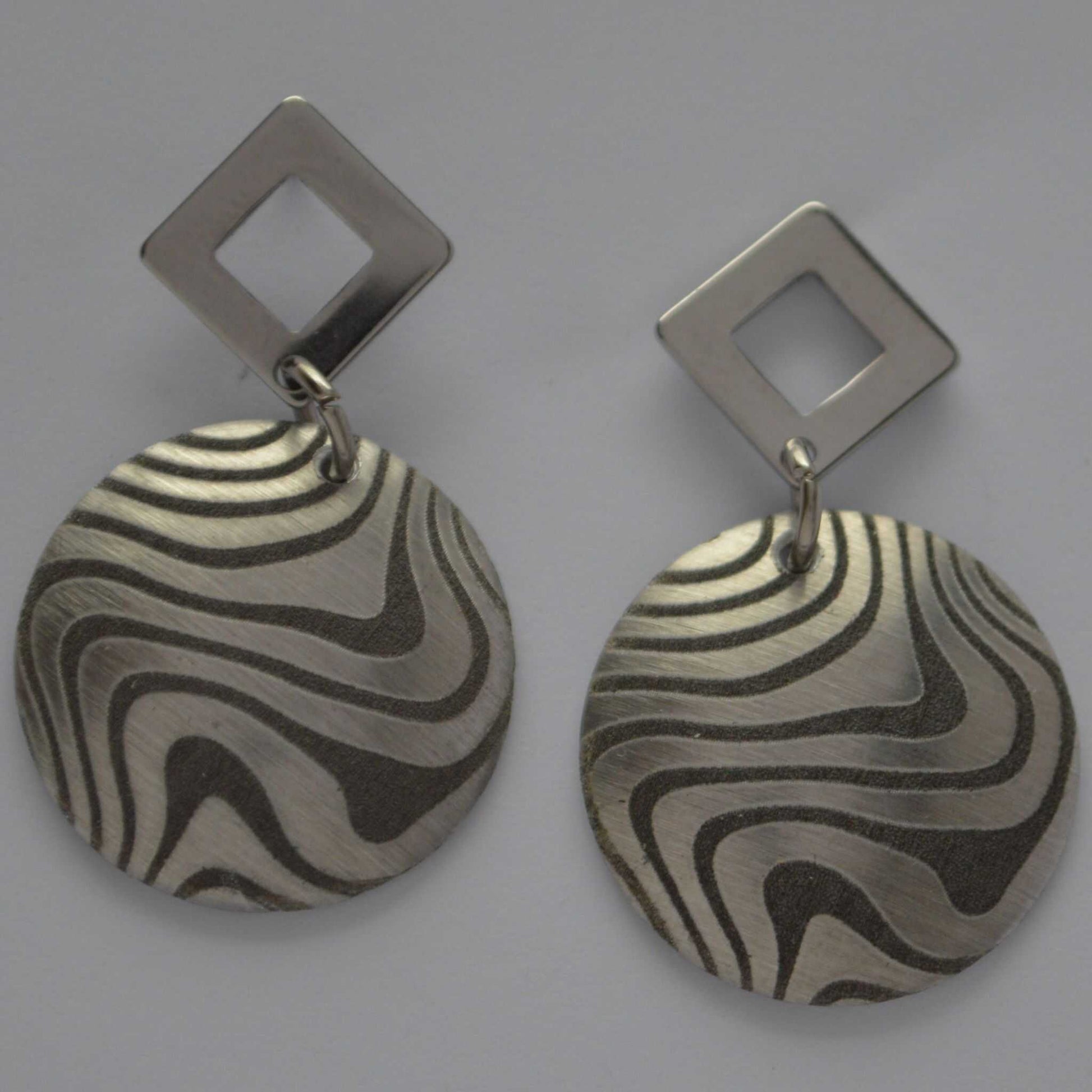 A pair of aluminum swirl design earrings with angled silhouettes, featuring a pattern of black and silver swirls.