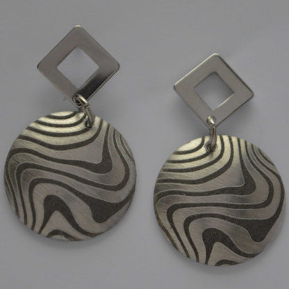 A pair of aluminum swirl design earrings with angled silhouettes, featuring a pattern of black and silver swirls.
