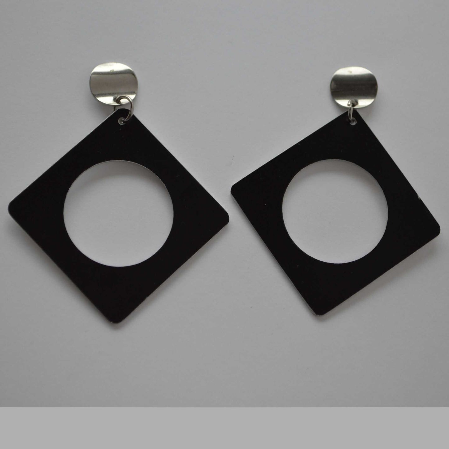 A pair of minimalist square earrings with a negative space design, crafted from black anodized aluminum, attached to silver colored findings.