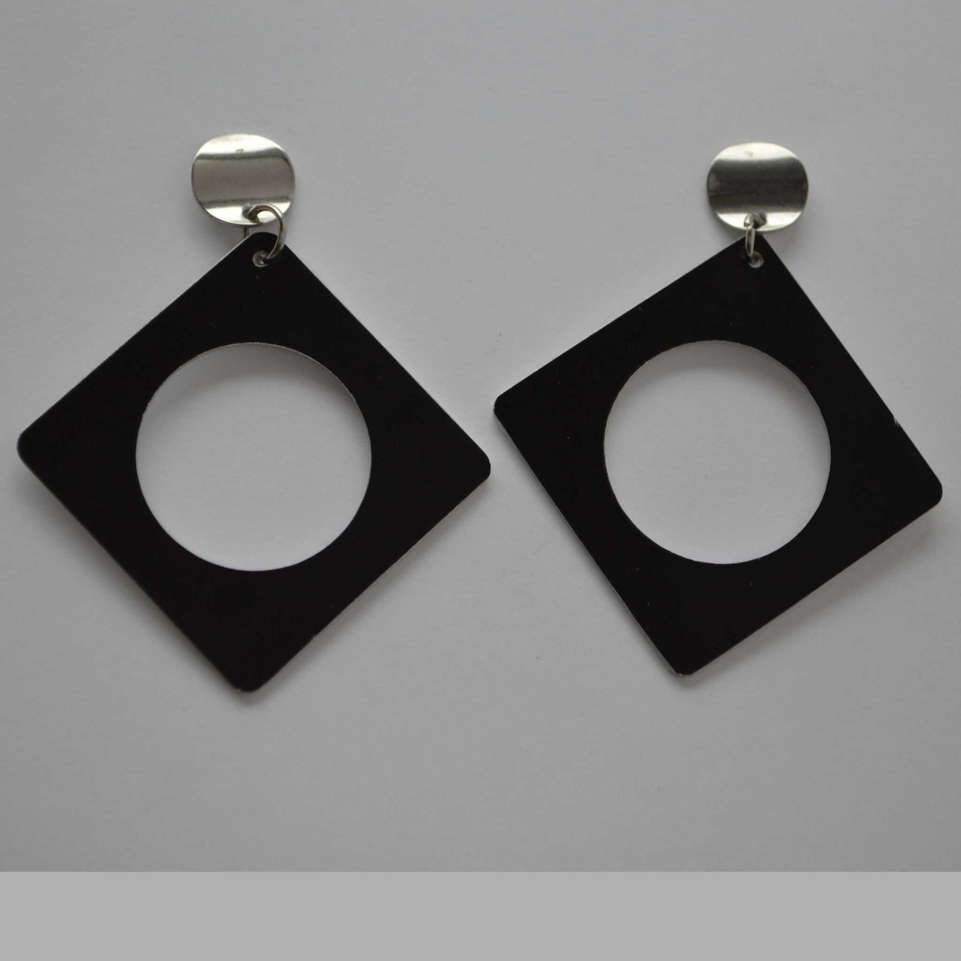 A pair of minimalist square earrings with a negative space design, crafted from black anodized aluminum, attached to silver colored findings.