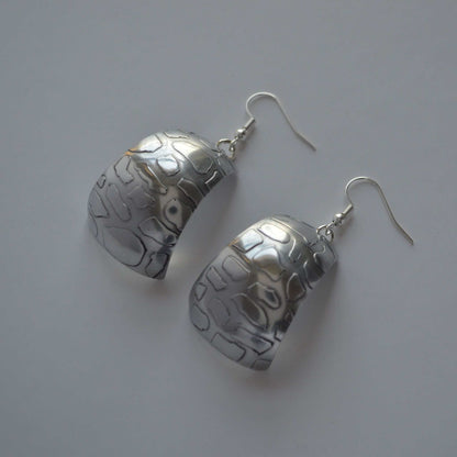 A pair of silver-colored aluminum earrings with a curved and patterned design.