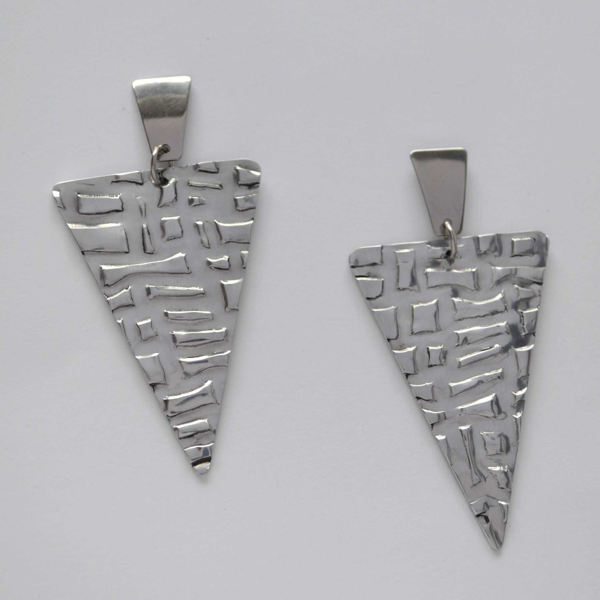 A pair of silver triangle earrings with a textured, artisanal stone-print pattern.